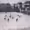 Match de hockey sur glace sur une patinoire extérieure entourée de spectateurs.