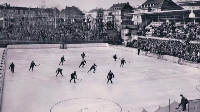 Match de hockey sur glace sur une patinoire extérieure entourée de spectateurs.